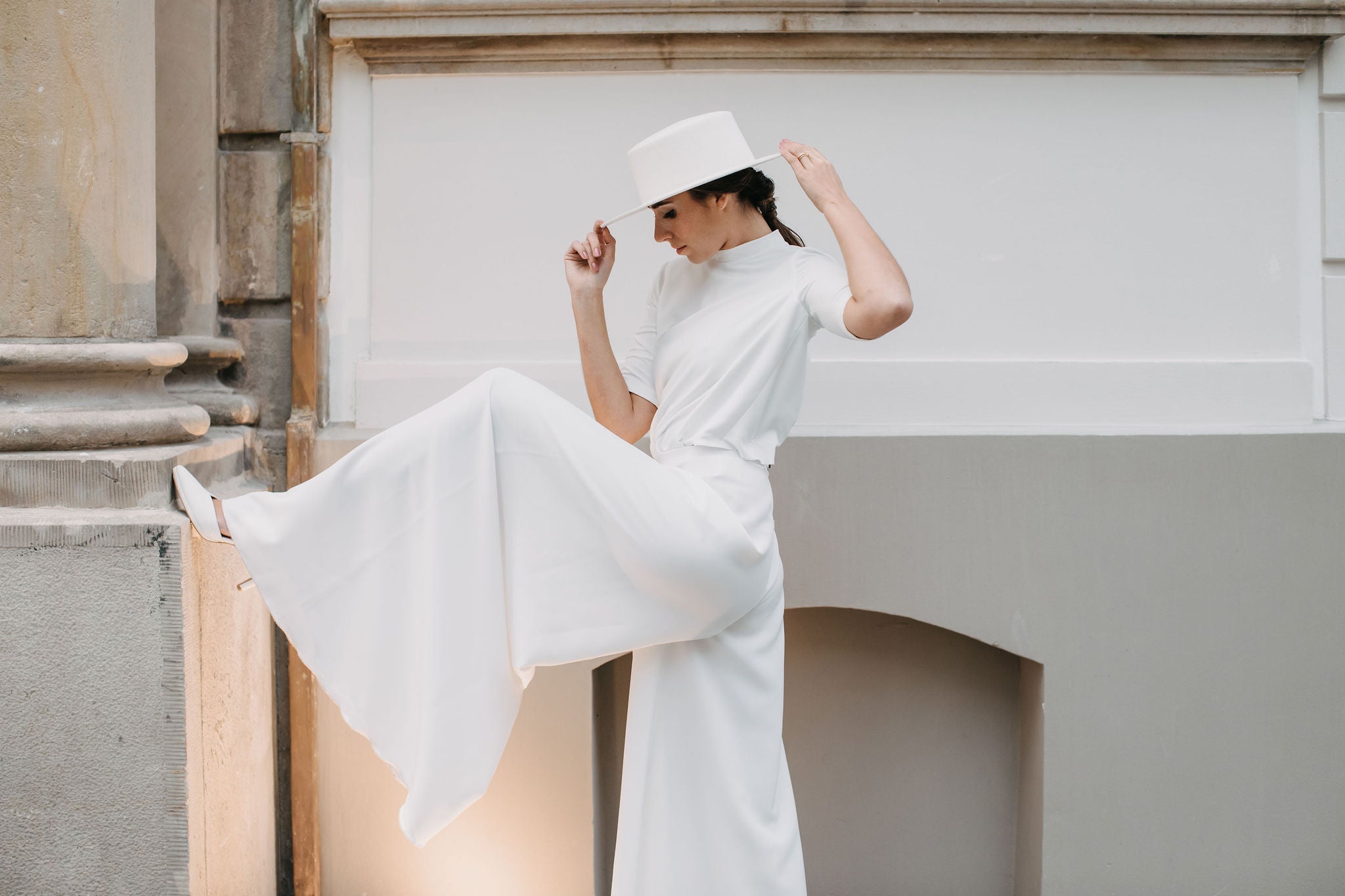 Stilvolle Frau in Weiß mit breitem Hut – zeitloser, reduzierter Hochzeitslook mit floraler Leichtigkeit