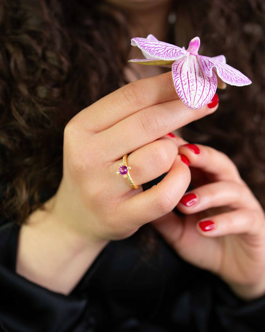 Hand hält Blume und trägt Gelbgold-Verlobungsring Rosa Saphir – nachhaltig aus Ceylon-Kollektion.