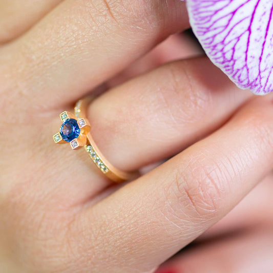 makroaufnahme von finger mit Gelbgold-Verlobungsring mit blauem Saphir und Diamanten – nachhaltig, hochwertig von Jan Spille