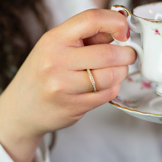 Frau hält teetasse und zeigt Gelbgoldener Pavé-Ring mit diamanten rundherum - fairtrade gold & faire diamanten