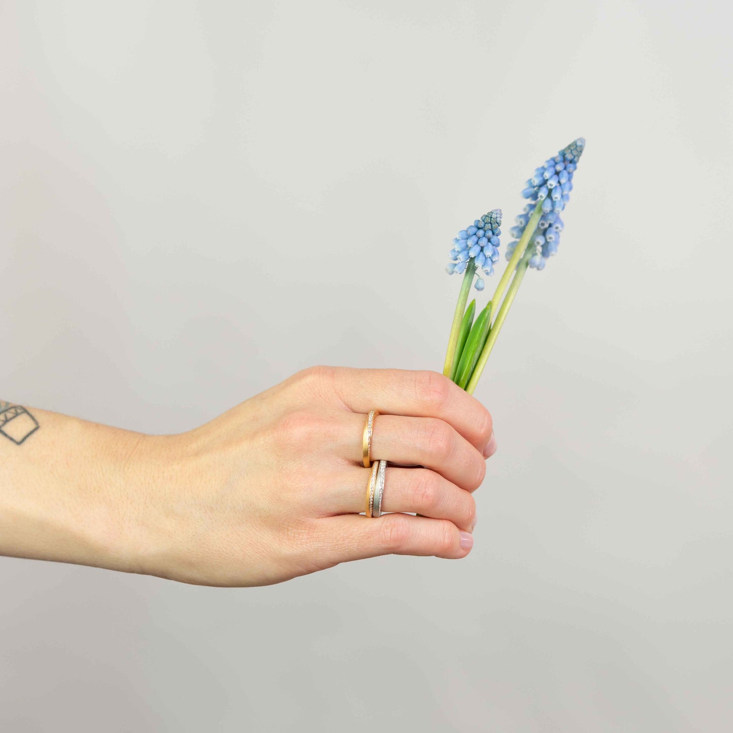 Hand hält Blume und zeigt handgefertigte gedrehte ringe aus 18 kt Gold – minimalistisches Design trifft Fairtrade-Schmuck.